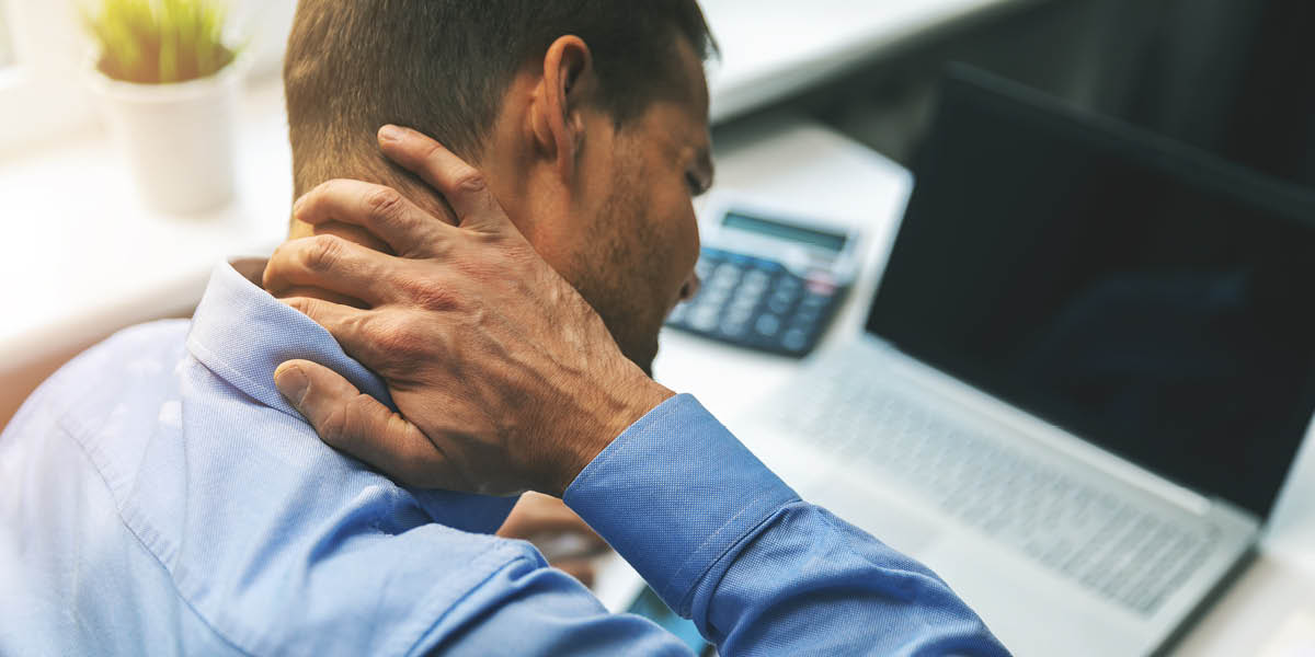 Pain Management - A man sitting at his desk rubbing his aching neck